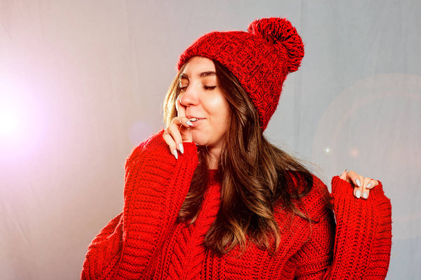 Красива, молода жінка в червоному в'язаному светрі і капелюсі на сірому ба
 - Фото, зображення