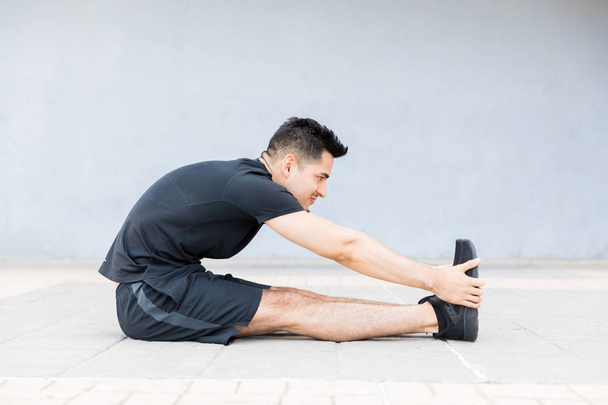 Мотивований і концентрований молодий чоловік розтягує ногу і робить ранкові вправи
 - Фото, зображення