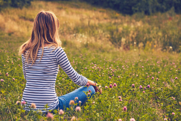 Κορίτσι κάθεται σε ένα καταπράσινο λιβάδι και βλέποντας την ύπαιθρο γη - Φωτογραφία, εικόνα