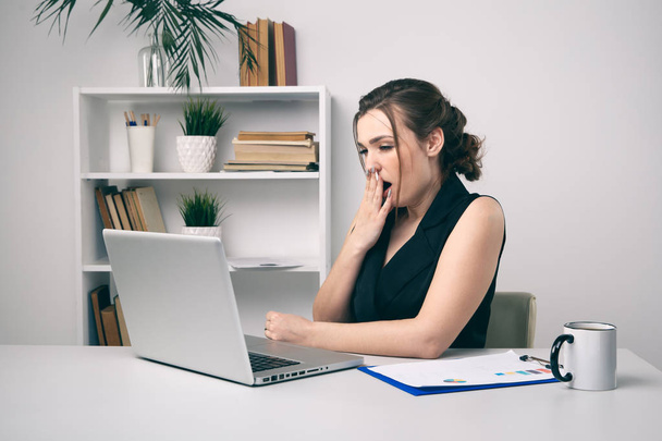 Sbadigliare giovane donna che lavora il suo computer portatile e bere caffè
. - Foto, immagini
