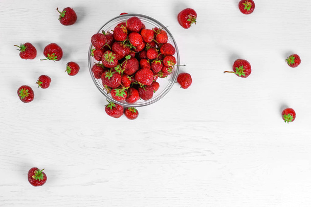 Heap of fresh strawberries in glass bowl on white wooden background. Top view - Photo, Image