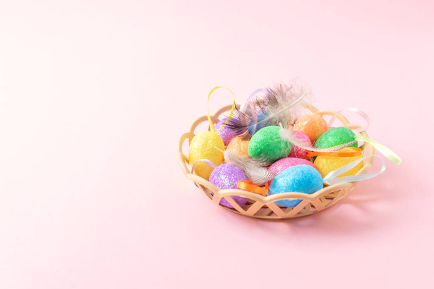 Декоративні великодні яйця з пір'ям в кошику на рожевому фоні
 - Фото, зображення