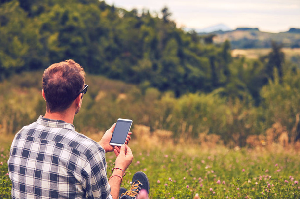 Mann benutzt Handy in der Natur auf einer Wiese. - Foto, Bild
