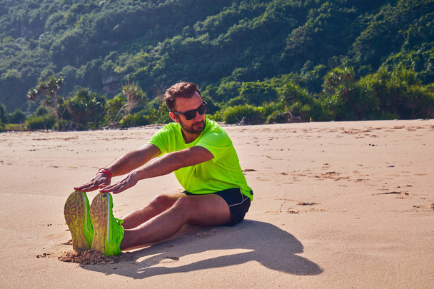 Sportivo che si estende su una spiaggia tropicale esotica dopo il jogging /
  - Foto, immagini
