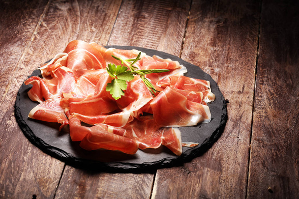 Italiaanse prosciutto crudo of jamon met rozemarijn. Rauwe ham op hout - Foto, afbeelding