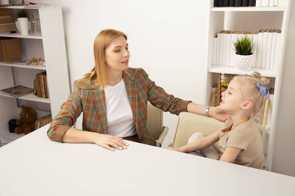 Madre con hija hablando entre sí sentada en el escritorio
. - Foto, Imagen