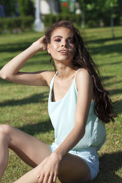 Young brunette woman in a turquoise blouse posing sitting on a g - Photo, image