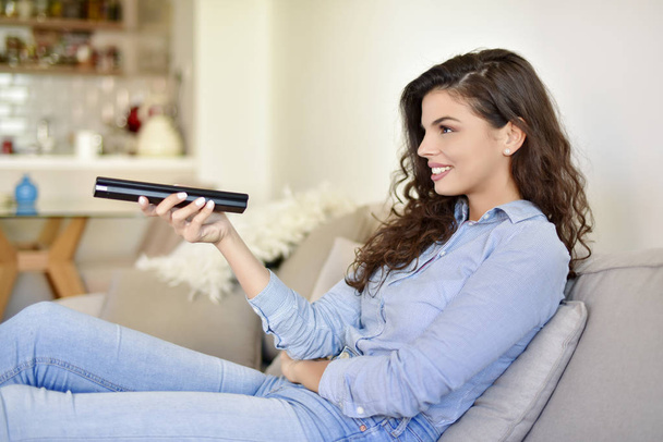 Young woman is holding the remote control and smiling - Fotoğraf, Görsel