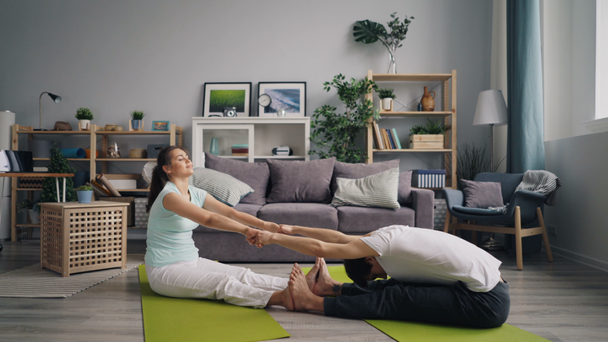 Ragazza e ragazzo che fa yoga stretching braccia, gambe e schiena a casa seduto su stuoie
 - Filmati, video