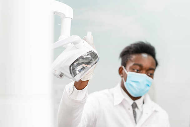 Νεαρός Αφρικανός οδοντίατρος σε οδοντιατρική κλινική. Ιατρική, υγεία, στοματολογία. οδοντίατρος που θεραπεύει ασθενή. - Φωτογραφία, εικόνα