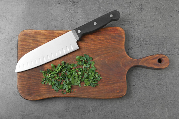 Wooden board with sharp knife and chopped parsley on grey background, top view - Foto, Imagen