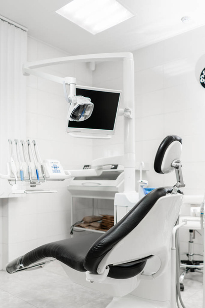 Вертикальний вид на стоматологічну кімнату з чорним сидінням. Сучасна стоматологічна практика. Стоматологічний стілець та інші аксесуари, що використовуються стоматологами
 - Фото, зображення