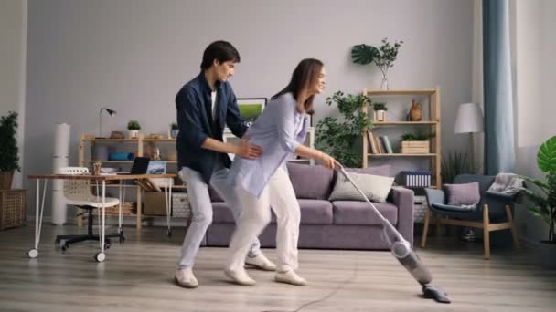 Loving couple vacuuming floor dancing laughing enjoying housework together - Materiał filmowy, wideo
