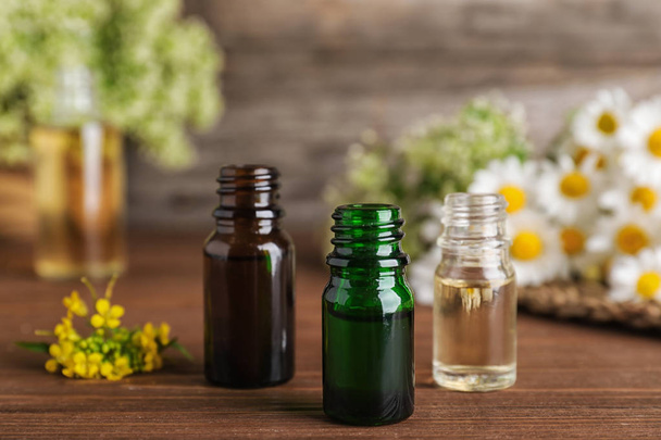 Bottles of essential oils with flowers on wooden table, space for text - Photo, Image