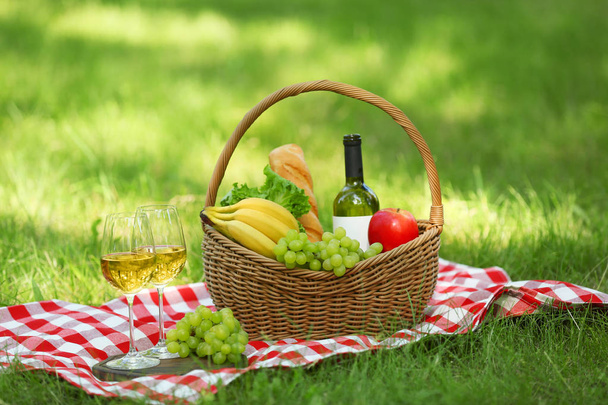 Wicker basket with food and wine on blanket in park. Summer picnic - Photo, Image