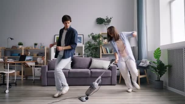 Young family dancing singing during housework using vacuum cleaner at home - Záběry, video