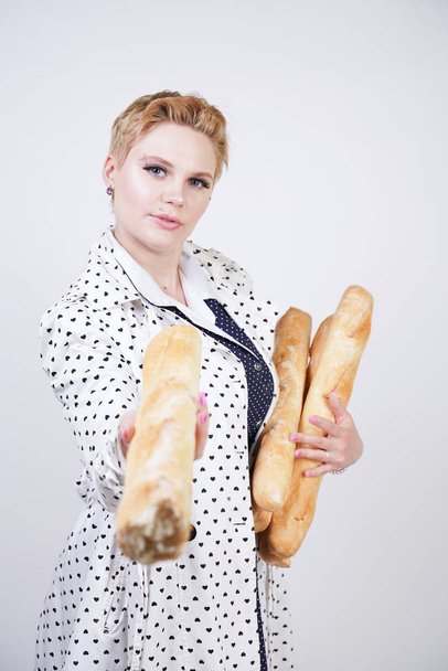 Urocza kobieta Pinup z krótkimi włosami w płaszcz wiosenny z kropkami stwarzających z bagietkami i korzystających z nich na białym tle w Studio. plus rozmiar dziewczyna w retro Odzież trzyma chleb. - Zdjęcie, obraz