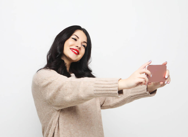 Fashion curvy brunette girl taking photo makes self portrait on smartphone - Φωτογραφία, εικόνα