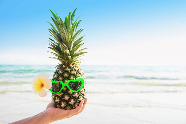 Lovely fresh pineapple putting glasses in tourist hands with sea wave background - happy fun with healthy vacation concept - Photo, Image