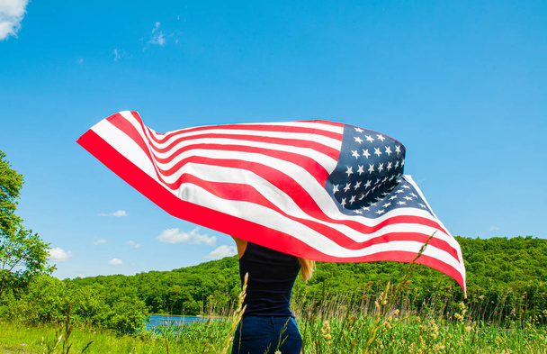 Young woman holding American flag on blue sky background. 4th of July - Foto, immagini