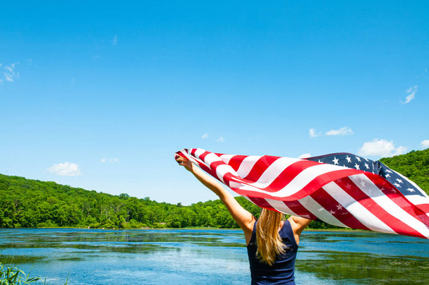 4th of July. Young woman holding American flag on lake background. - Fotó, kép