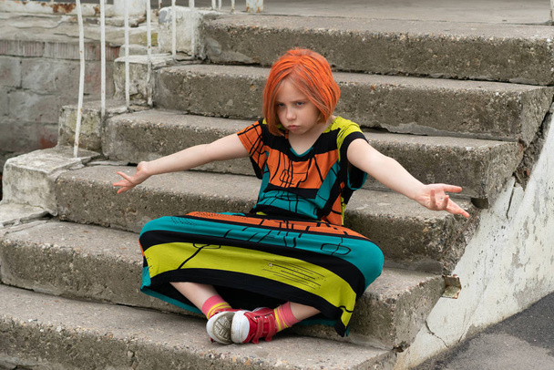 little girl sitting on the stairs in a colored dress - Foto, Imagen