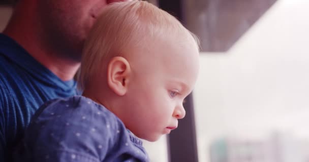 Close up shot of father and baby daughter looking out glass window of apartment in city  - Záběry, video