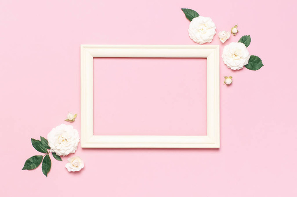 Flowers composition. Wooden white photo frame, white fresh roses and green leaves on gentle pink background. Flat lay, top view, copy space. Flower card, greeting, holiday mockup. Valentine's Day - Foto, immagini