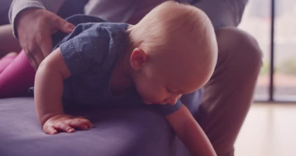 Young happy baby girl crawling and playing on couch with dad in background in modern apartment - Materiał filmowy, wideo
