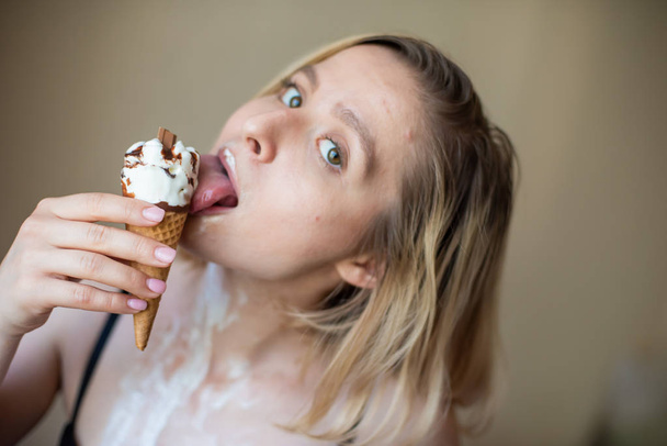 Sexy blonde licks a waffle cone. Ice cream is melting, erotically draining through the body of an attractive woman. Beautiful girl smeared with ice cream. - Φωτογραφία, εικόνα