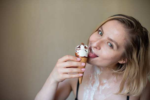 Sexy blonde licks a waffle cone. Ice cream is melting, erotically draining through the body of an attractive woman. Beautiful girl smeared with ice cream. - Foto, immagini