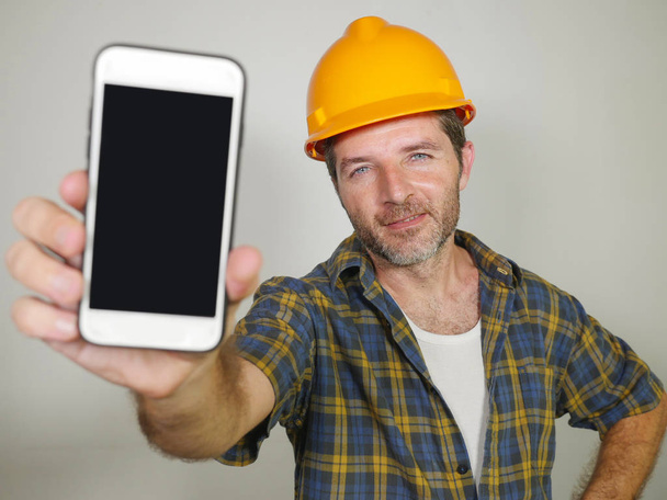 constructor worker in contractor helmet holding mobile phone offering company building and repair services smiling cheerful and confident inviting for calling - Foto, imagen