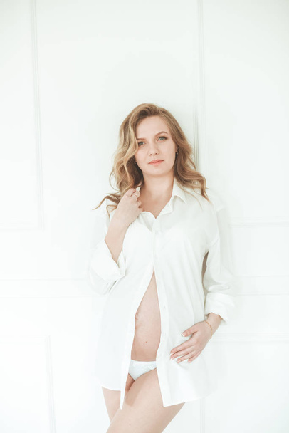 Young beautiful pregnant woman Belly of a pregnant woman. Cute pregnant belly. Beautiful pregnant woman blonde in white lace Peignoir. Girl in white lingerie - Foto, Bild