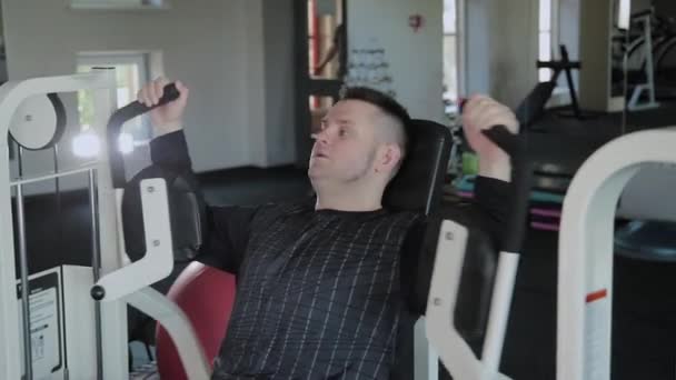 Adult man with excess weight trains his chest on the simulator. - Záběry, video
