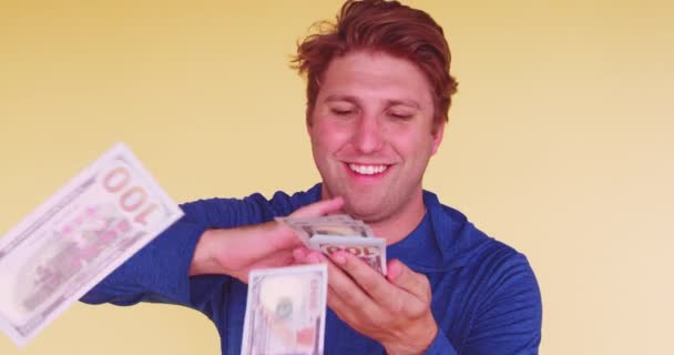Young happy millennial throwing money at camera on yellow colored background  - Πλάνα, βίντεο