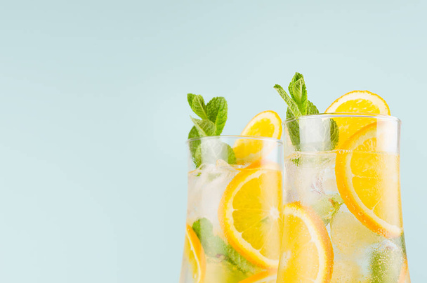 Healthy fresh oranges cocktail with sliced fruit, ice cubes, green mint on elegant soft blue color wall, closeup, top section, edge. - Photo, image