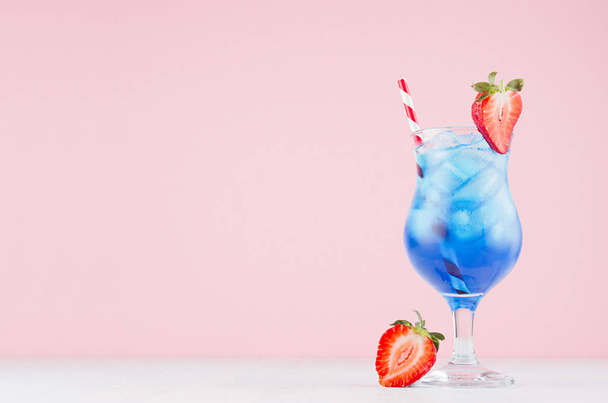 Blue beach cold alcohol drink with curacao liquor, ice cubes, strawberry in elegant wineglass on pastel pink background. - Foto, imagen