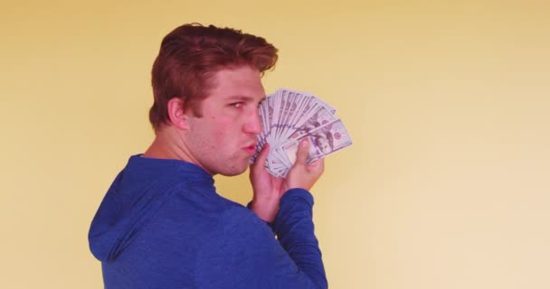 Young millennial fanning himself with money on bright colored background in studio - Materiał filmowy, wideo