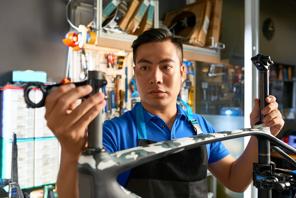 Hombre asiático de pie en el delantal y recoger la nueva bicicleta en el taller de reparación
 - Foto, Imagen