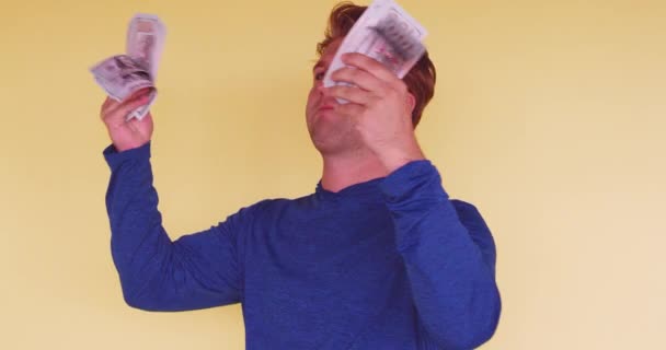 Young funny millennial waiving himself with money on bright colored background  - Кадри, відео