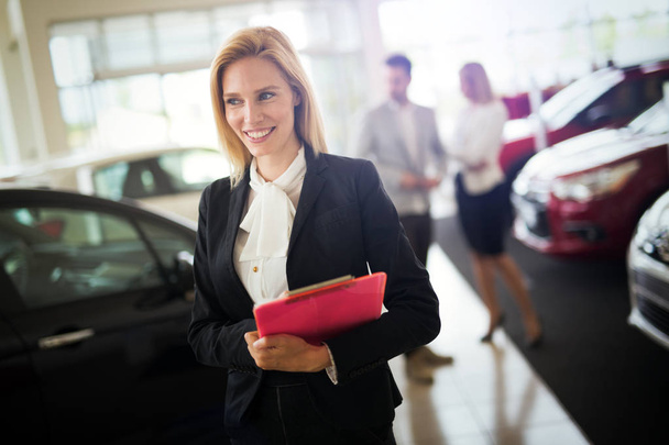 Portrait of beautiful young saleswoman standing inside vehicle showroom - Photo, Image