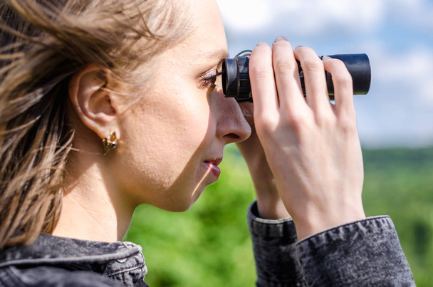 Een vrouw met verrekijker in haar handen kijkt naar de afstand in het wild, jagen, kijkend naar een betere toekomst. - Foto, afbeelding