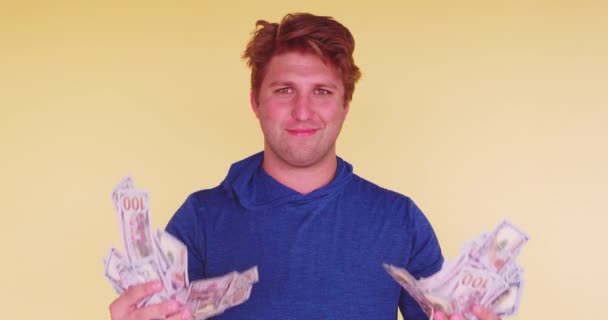 Young funny millennial waiving himself with money on bright colored background  - Footage, Video