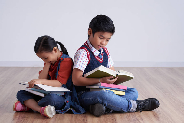 Twee klasgenoten zittend op de vloer terug naar terug lezen boeken en voorbereiding voor de les - Foto, afbeelding