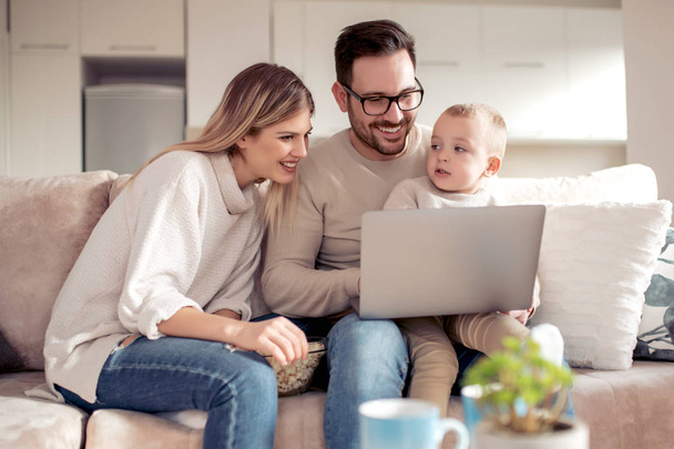 Χαμογελώντας τους γονείς και τους μικρό γιο που χρησιμοποιούν φορητό υπολογιστή στο σπίτι. - Φωτογραφία, εικόνα