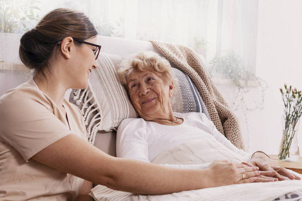Elderly woman in hospital bed with social worker helping her - Фото, зображення