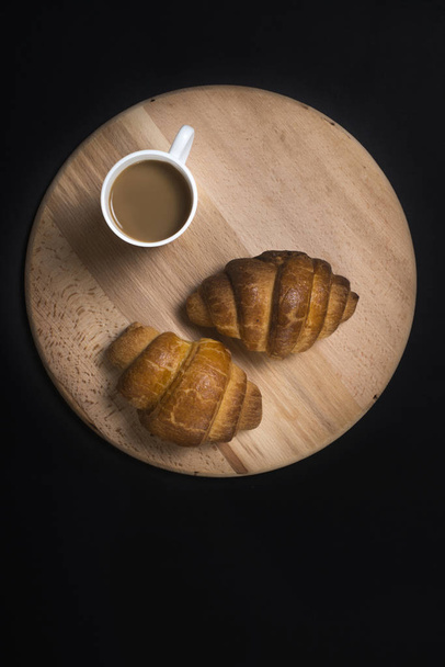 Freshly baked croissants on wooden board with cup of coffee on b - Fotó, kép