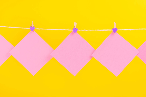 Pink stickers on clothesline with clothespins isolated on yellow background. Place for your text. - 写真・画像