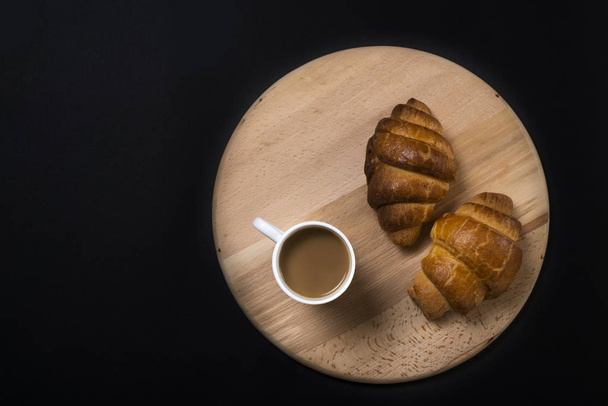 Freshly baked croissants on wooden board with cup of coffee on b - Foto, afbeelding