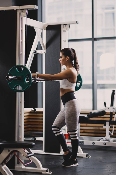 Athletic girl dressed in sportswear is going to lift weight in the modern gym - Фото, изображение
